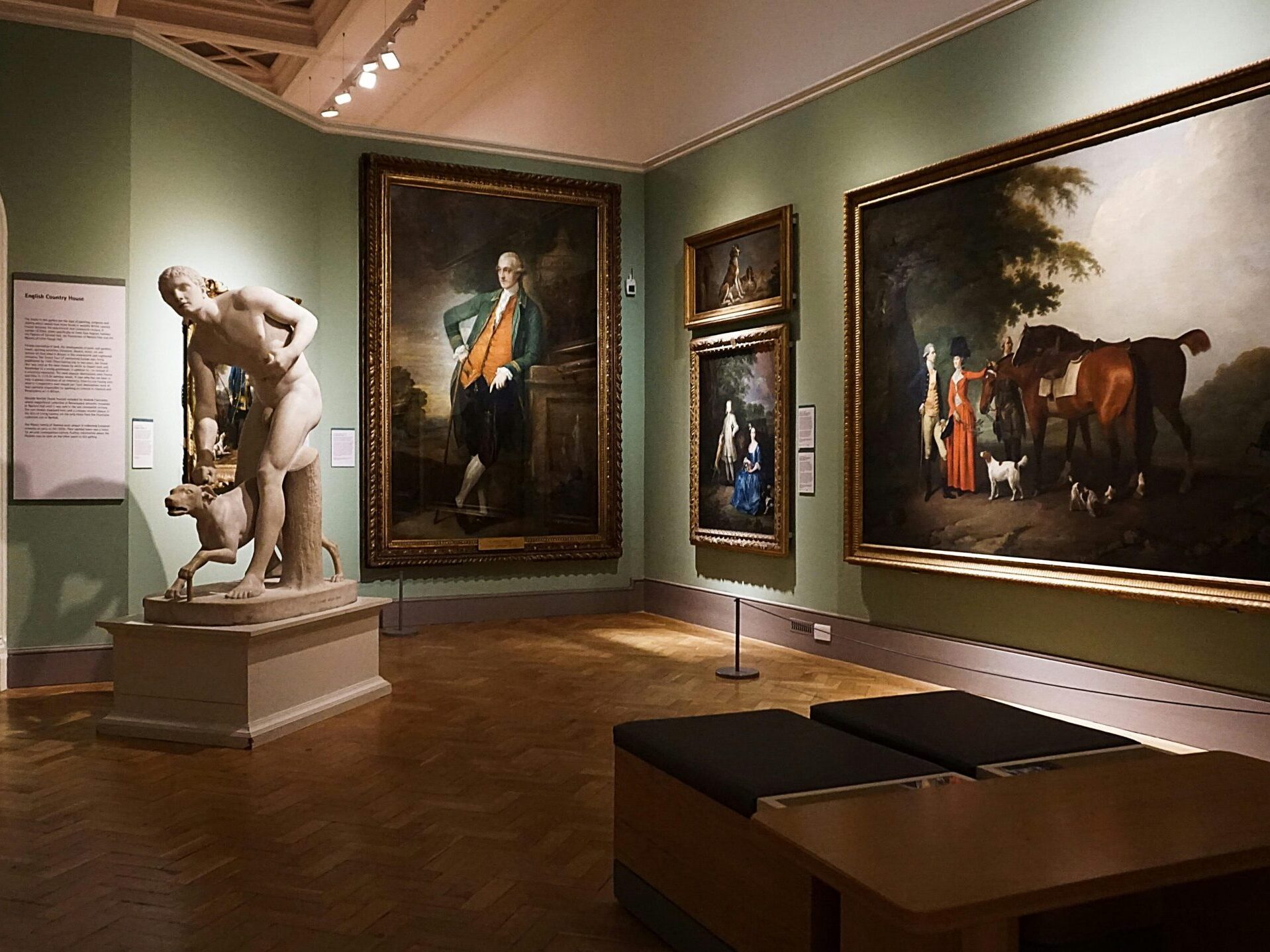 An elegant art gallery room featuring classical paintings and a prominent marble statue.